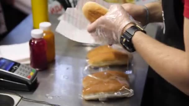 Muž dává chutné klobásy do čerstvé housky vaření hotdog v kavárně — Stock video