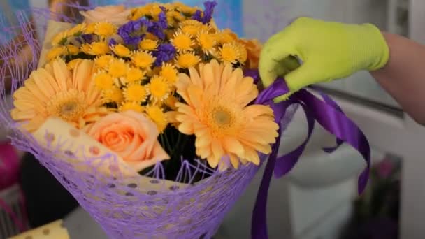 Флорист в рукавичках налаштовує фіолетову стрічку на букет в магазині — стокове відео