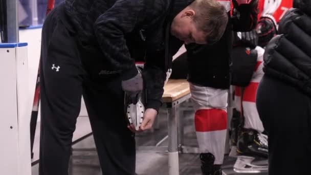 Trainer stellt Schlittschuh von Hockeyspieler nahe Holzbank ein — Stockvideo