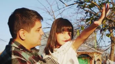 Mutlu bir baba kızını sabah köy bahçesinde tutuyor.