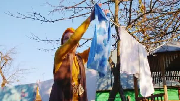 Lady in yellow clothes hangs towel on rope in house yard — Stock Video