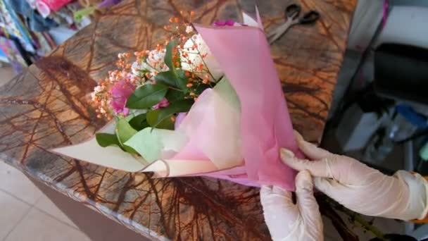 Virágüzlet gumikesztyűben virágcsokor rózsaszín fóliával — Stock videók
