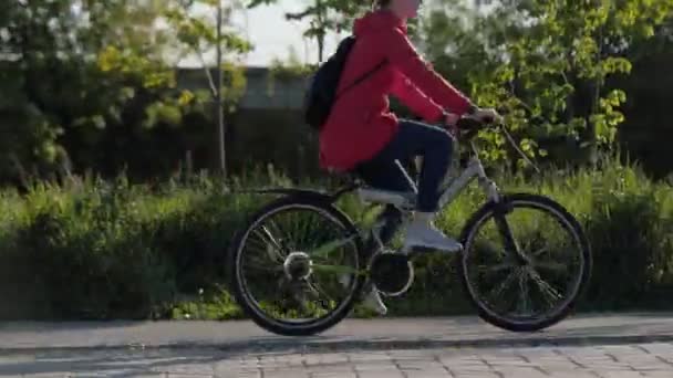 Молодая леди в красной куртке ездит на велосипеде по зеленому парку — стоковое видео