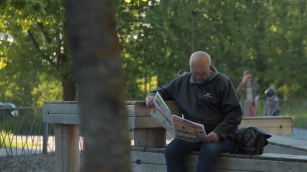 Senior avec des lunettes lit journal sur banc dans le parc — Video