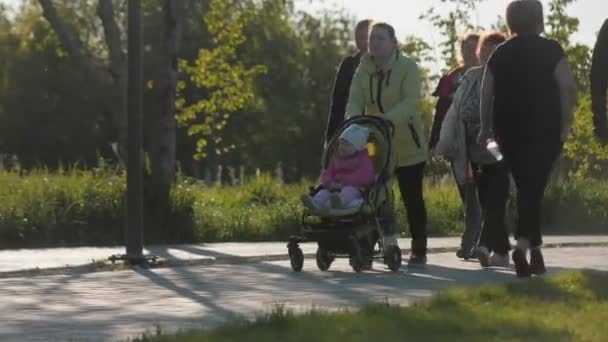 Мама и бабушка гуляют с ребенком в мешочке вдоль зеленого сада — стоковое видео