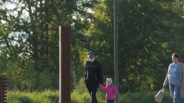 Hombre en máscara protectora camina con niña a lo largo del jardín — Vídeo de stock