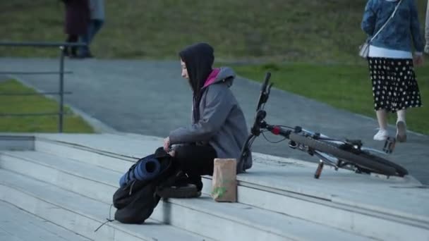 Mujer joven con mochila y bicicleta se sienta en los escalones del parque — Vídeo de stock