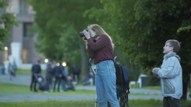 Женщина фотографируется с камерой возле мешка в зеленом парке — стоковое видео