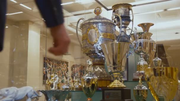 Hombre mira brillantes copas ganadoras de deportes en escaparate de cristal — Vídeo de stock