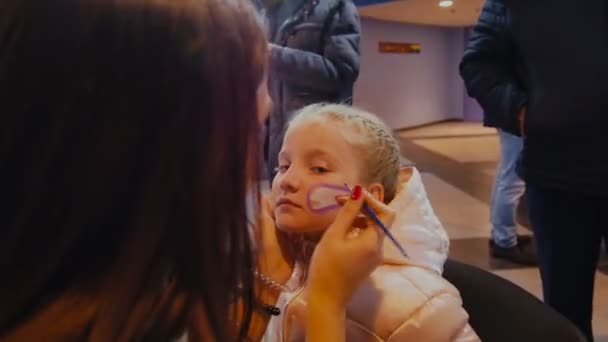 Mujer dibuja en cara de niña con colores púrpura blanco en la sala — Vídeo de stock