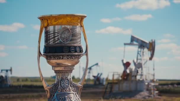 Golden and yellow cup against large pump jacks in oil field — Stock Video