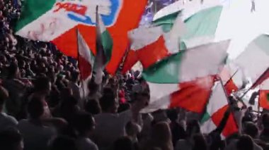 Modern stadyumda takım logosu olan spor taraftarı bayrakları sallıyor