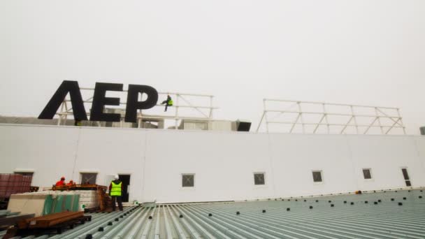 Zespół pracowników instaluje logo sklepu Leroy Merlin na dachu — Wideo stockowe