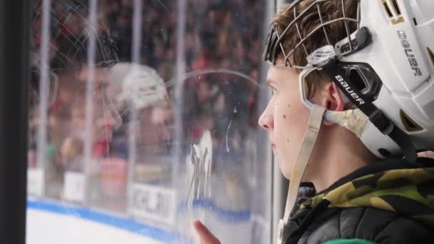 Teenage boy in helmet watches hockey game near ice arena — Stock Video