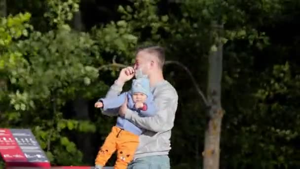 Papa dans le masque porte petit bébé dans les bras marchant le long du parc — Video