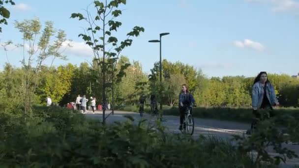 Девушки ездят на велосипедах по дорожке в парке с отдыхающими людьми — стоковое видео