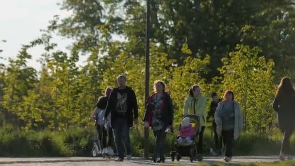 Kinderen rijden scooters en mensen lopen langs de weg in de tuin — Stockvideo