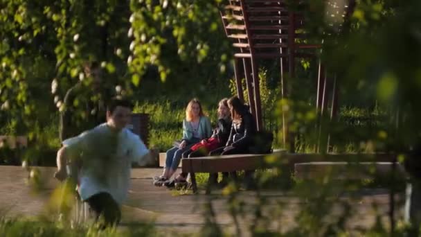 Genç kızlar grup konuşmaları parktaki ahşap bankta oturuyor. — Stok video
