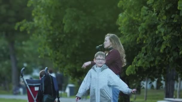 Kvinna tar bild nära pojke med glasögon i grön trädgård — Stockvideo