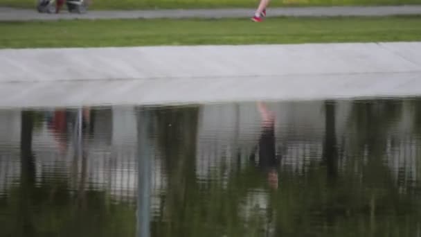 Young man runs along lawn near tranquil pond in city park — Stock Video
