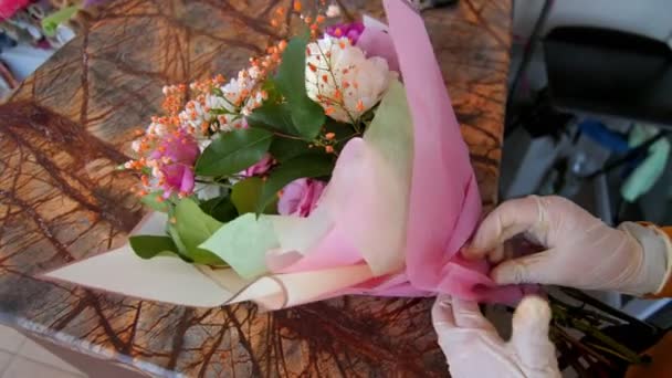 Kvinna lindar färsk blombukett med rosa folie vid bordet — Stockvideo