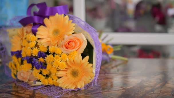 Oranžová kytice zabalená s fialovými oky na stole — Stock video