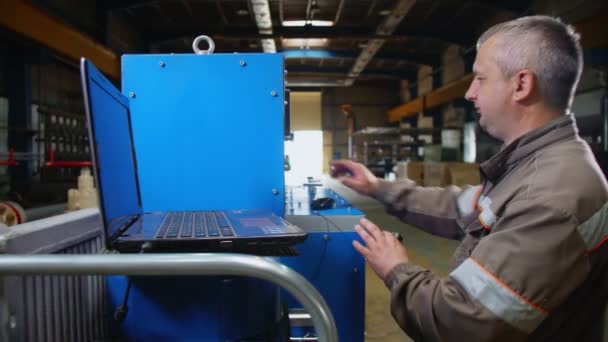 Зрелый рабочий работает с панелью управления станком и ноутбуком — стоковое видео