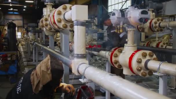 Arbeiter in Maske schweißt Pipeline, während Kollege telefoniert — Stockvideo