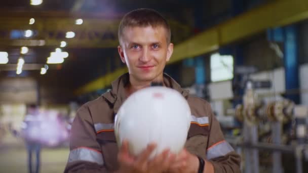 Счастливый человек в серой форме надевает белый шлем в мастерской — стоковое видео