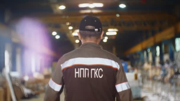 Trabajador maduro en logotipo chaqueta uniforme camina a lo largo del taller — Vídeos de Stock