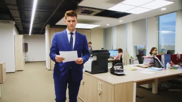 Человек с печатными документами беседует с коллегой, входящим в офис — стоковое видео