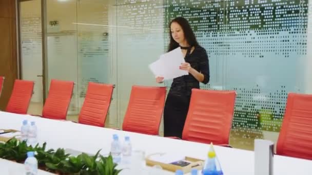 Biuro asystent w czarnej sukience kładzie papiery na stole spotkań — Wideo stockowe