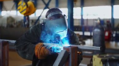 Sakallı işçi kaynakçıları ve metal iskeletin yanındaki maskeyi çıkarıyor.