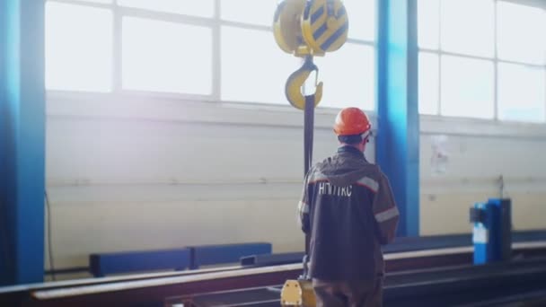 Laborer in orange helmet controls large hook with magnet — Stock Video
