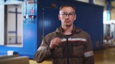 Üniformalı adam elektrik santralinin yakınında gözlüklerini çıkarıyor.
