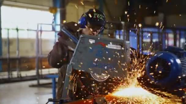Mitarbeiter mit Kopfhörer schneidet Metalldetail in Werkstatt — Stockvideo