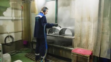 Kulaklıklı işçi metal detayları buharla temizliyor