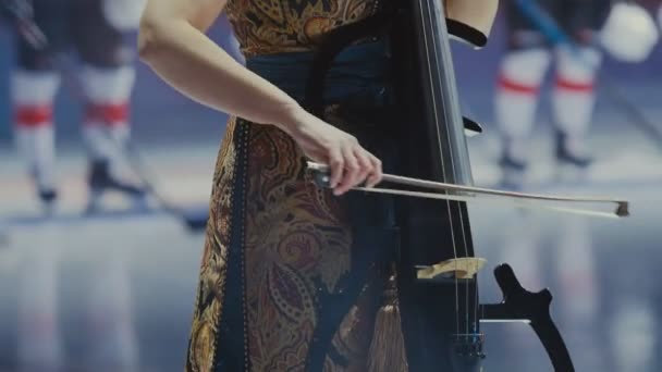 Woman in elegant dress plays cello against hockey players — Stock Video