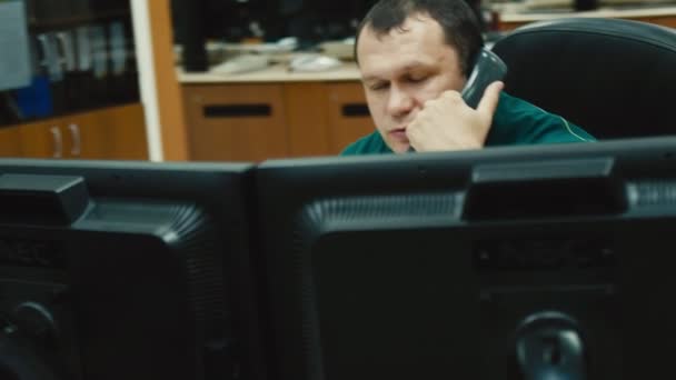 Сотрудник говорит по телефону сидя за столом с компьютером — стоковое видео