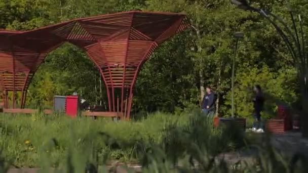 在绿色的春天公园里，女人走过时尚的木制凉亭 — 图库视频影像