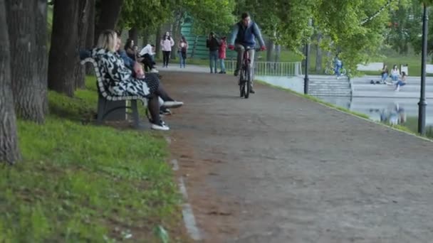 Ung mand rider cykel langs sporet nær rolig dam i park – Stock-video