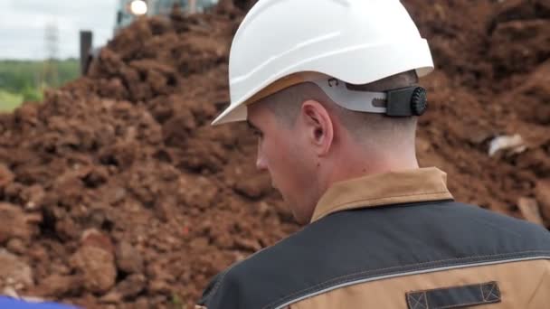 Мастер в шлеме разговаривает с рабочим, копающим траншею в земле — стоковое видео