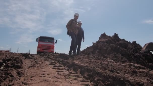 Мужчины в хардхатах спускаются с холма к красному грузовику. — стоковое видео