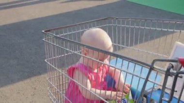 Bebek elbiseli kız otoparkta alışveriş arabasında oturuyor.