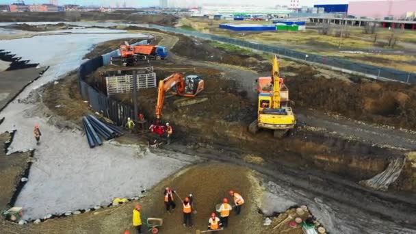 Экскаваторы копают землю под контролем рабочих при строительстве — стоковое видео
