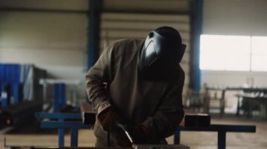 Üniformalı adam atölyedeki metal parçaları kaynak yapmak için maske takıyor.