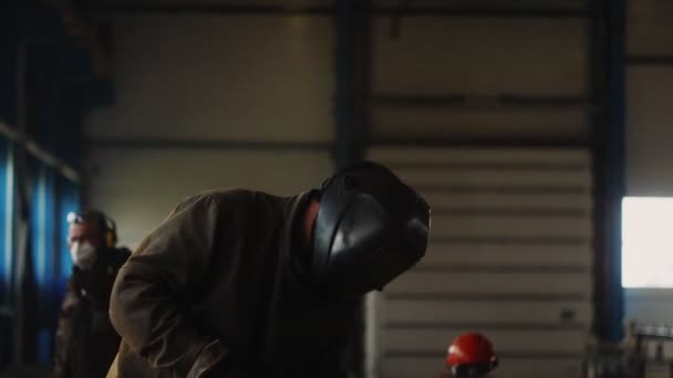 Maskeli işçi, atölyedeki kıvılcımlarda metal parçaları kaynaklıyor. — Stok video