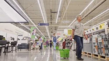 Müşteriler geniş süpermarket salonlarında mal seçerek yürür.