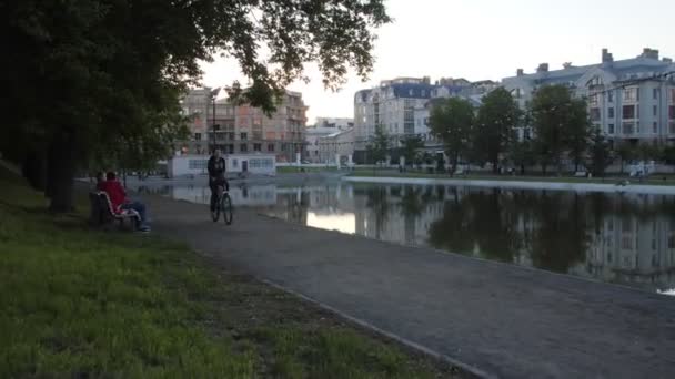 Жінка їздить на велосипеді по дорозі біля ставка в сучасному місті. — стокове відео