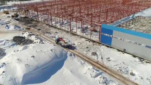 Вантажівки біля червоної туші майбутнього сховища на засніженому майданчику — стокове відео